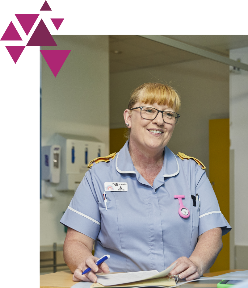 A smiling female nurse with glasses and a badge stands at a counter in a hospital, holding a pen and clipboard, wearing a uniform with epaulettes. pink and purple triangles decorate the top left corner.
