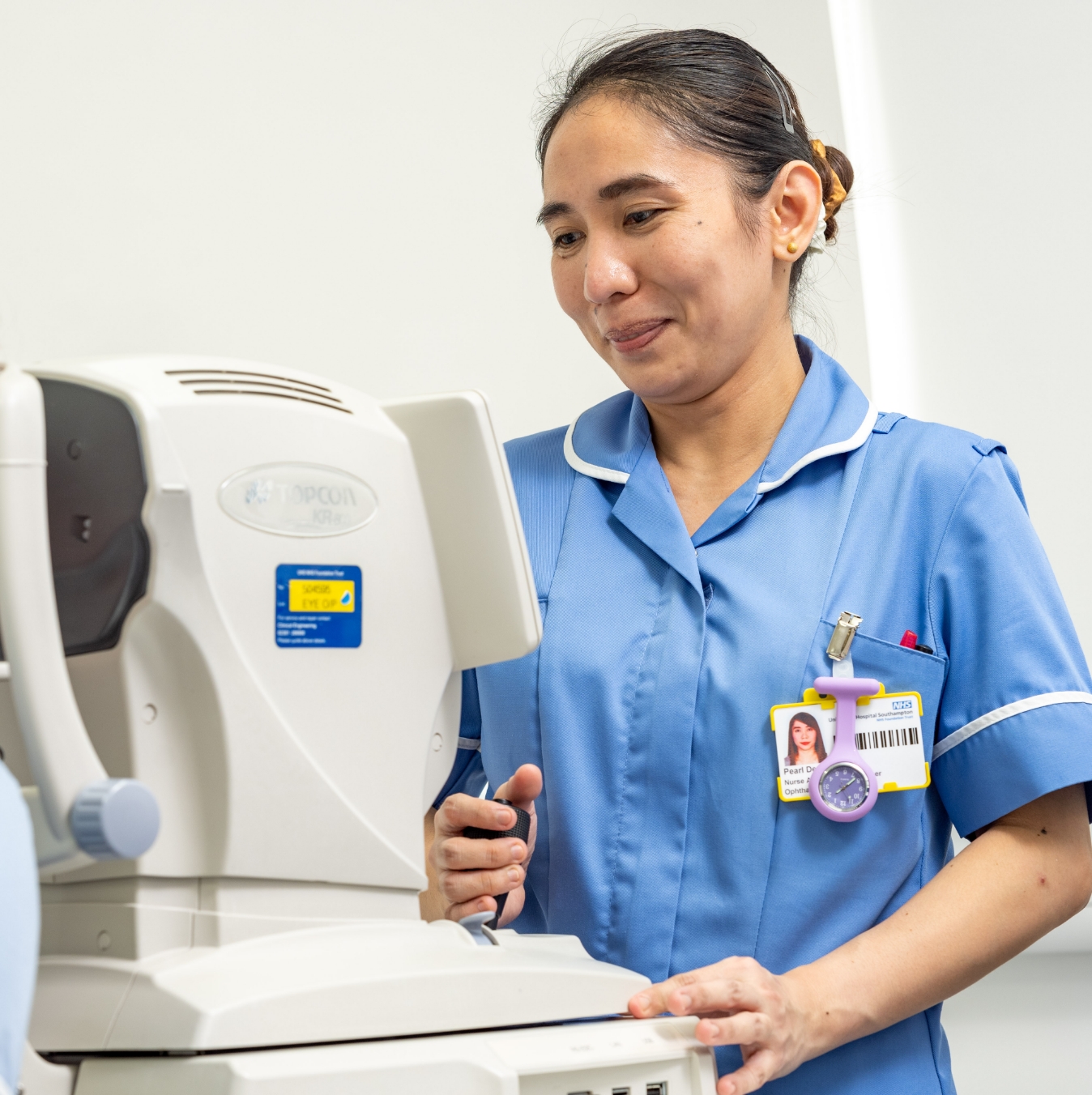 A female nurse in blue scrubs operating an eye examination machine, focusing attentively on her task.